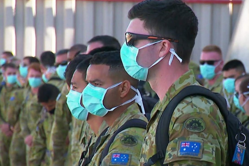 ADF officers lined up on arriving in Melbourne wearing blue surgical masks.