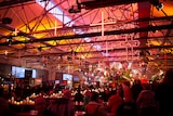 People sit at tables covered with candles and crosses overhead.