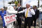 John Howard shakes hands with a person dressed in a polar bear suit holding a sign saying "fighting for survival".