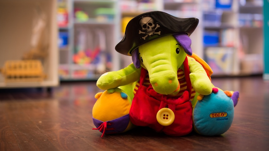 A brightly coloured toy elephant wearing a black plastic pirate hat sits on a wooden floor.