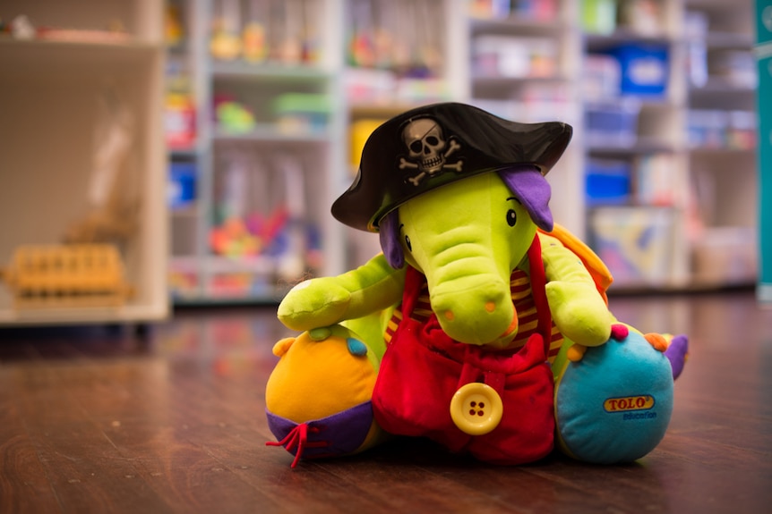 A brightly coloured toy elephant wearing a black plastic pirate hat sits on a wooden floor.