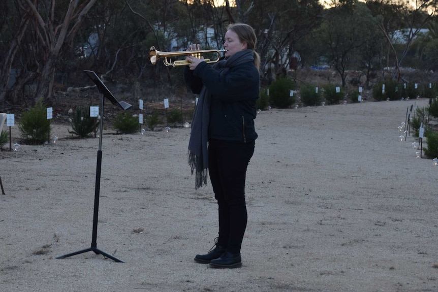 A woman, standing alone, playing a trumpet.