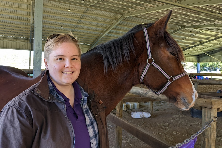 A smiling woman standing next to a horse