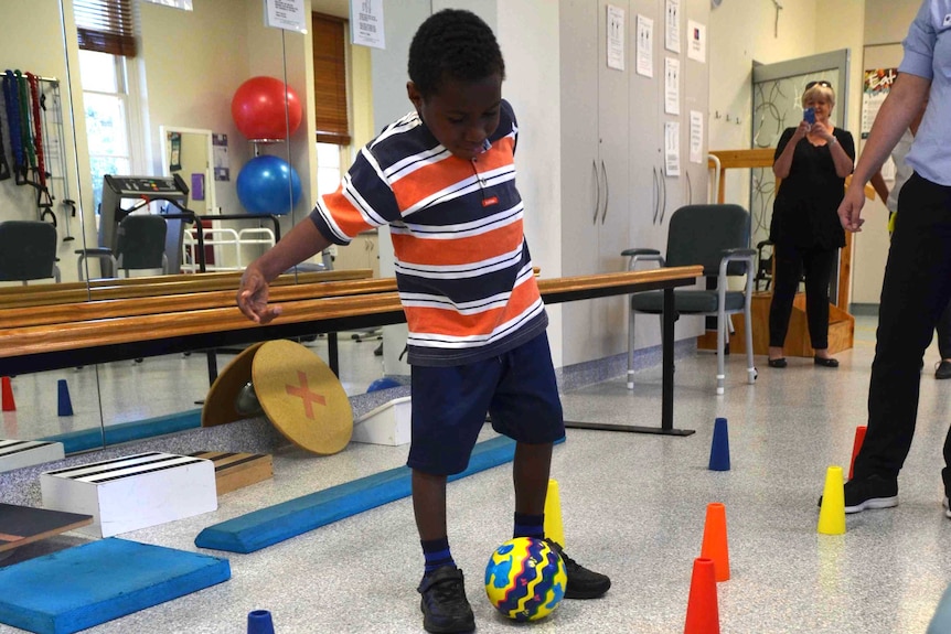 Edward, from PNG kicks the soccer ball around cones.