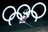 A skiier upside down in front of the Olympic rings.