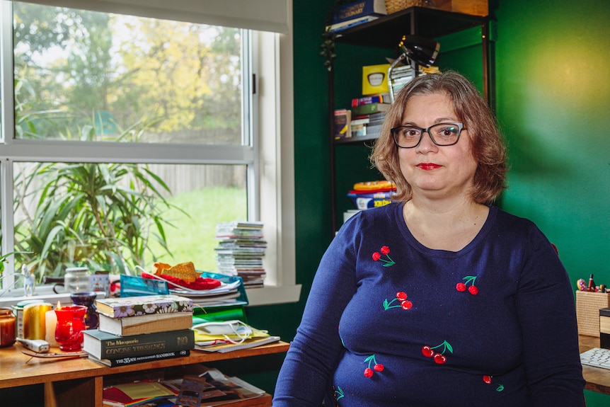 A woman with glasses and a blue top sitting by a window