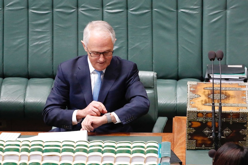 Malcolm Turnbull glances down to his left wrist and adjusts his watch with his right hand.