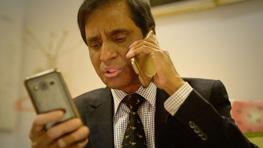 Abul Kalam holds a phone to his ear while also looking at a mobile phone he is holding with his other hand.