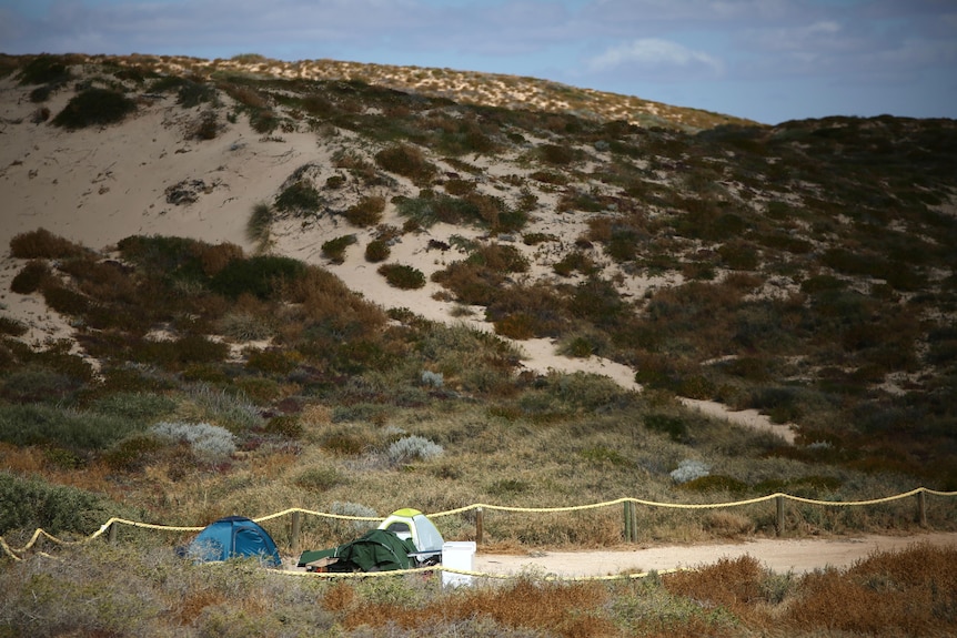 A wide shot of a group of tents in front of sand dunes.