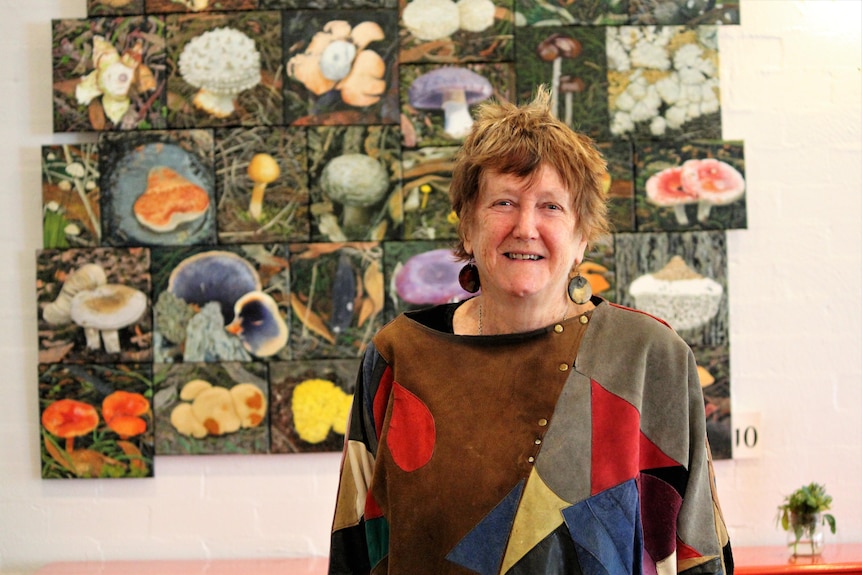 A woman stands in front of a panel of colourful fungi paintings