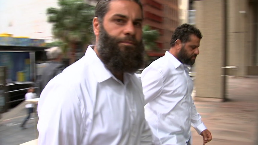 Two men in white shirts look at the camera while entering a court building