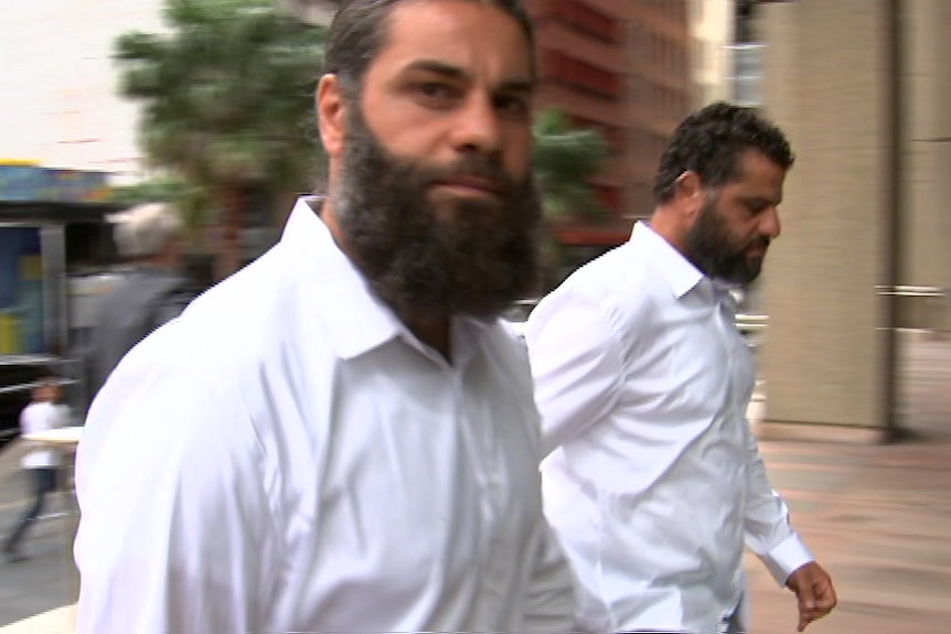 Two men in white shirts look at the camera while entering a court building