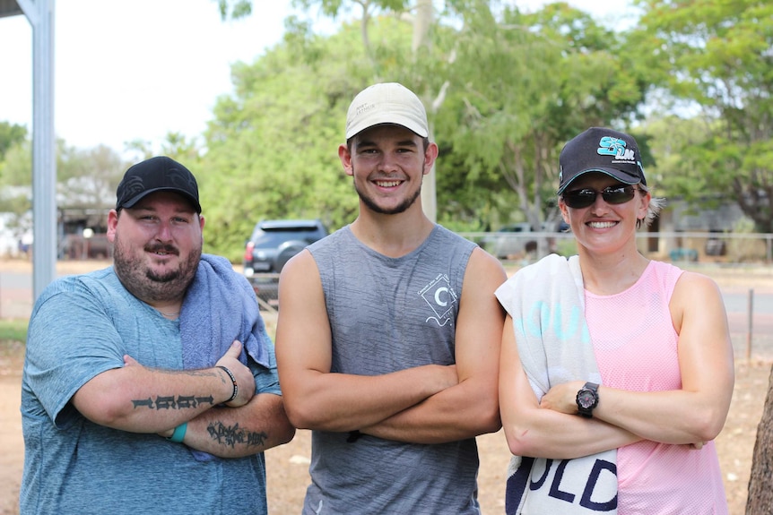 Two men and a woman in workout wear with their arms crossed standing outside a park.