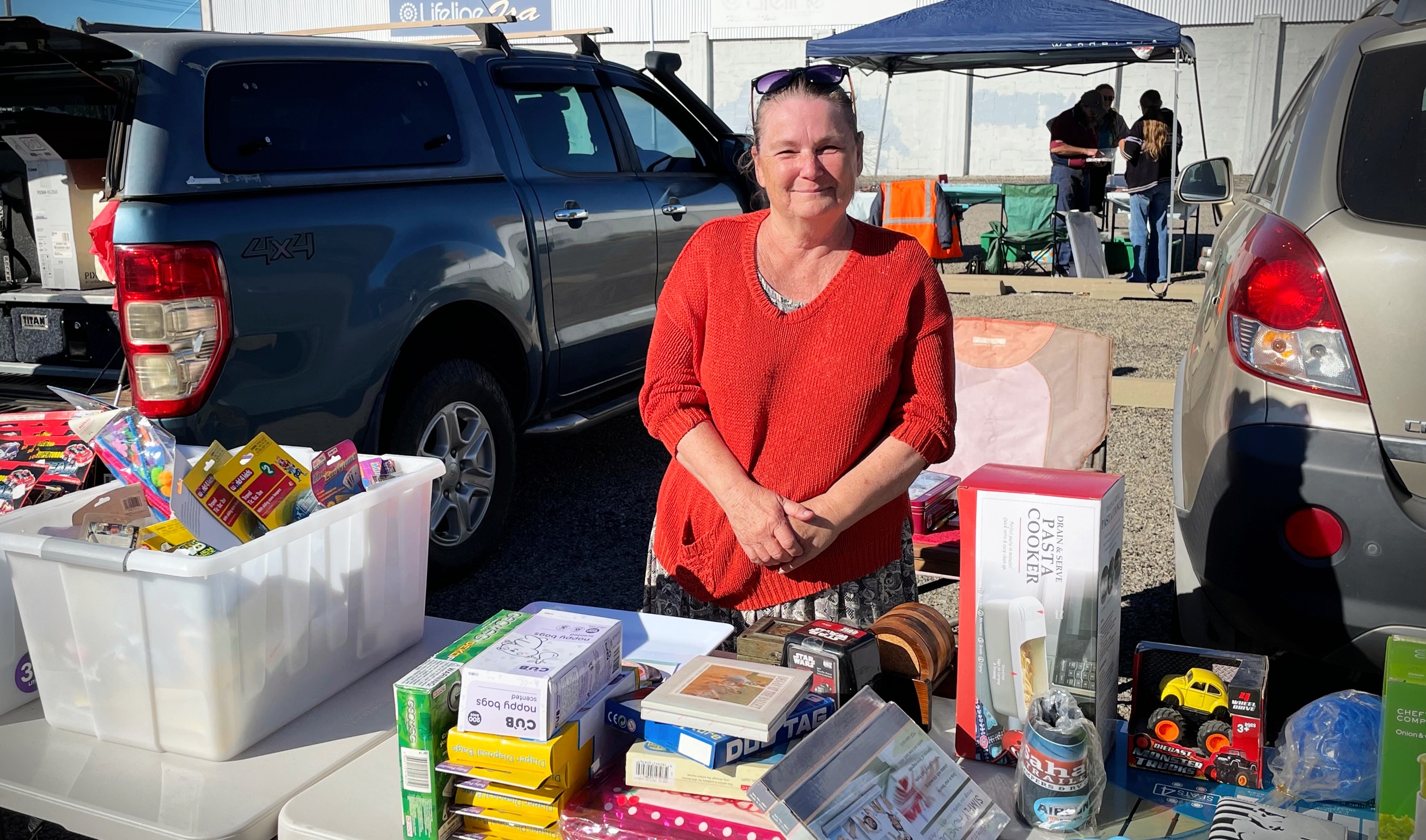 A woman in a red shirt stands behind a market stall smiling