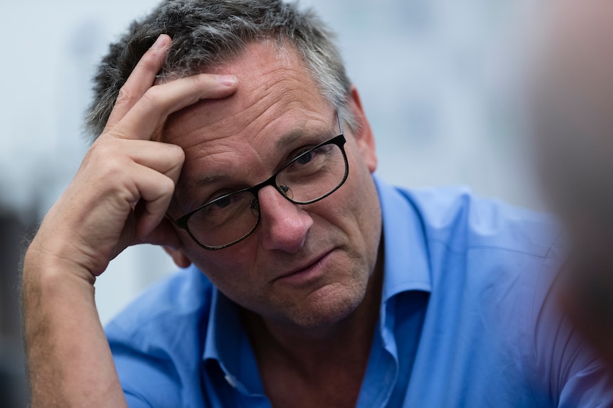 A close-up of Dr Michael Mosley talking while leaning his head on his right hand.