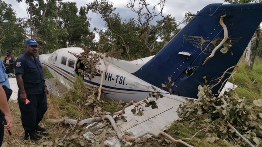 A man in police uniform stands next to a crashed plan in the bush.