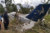 A man in police uniform stands next to a crashed plan in the bush.