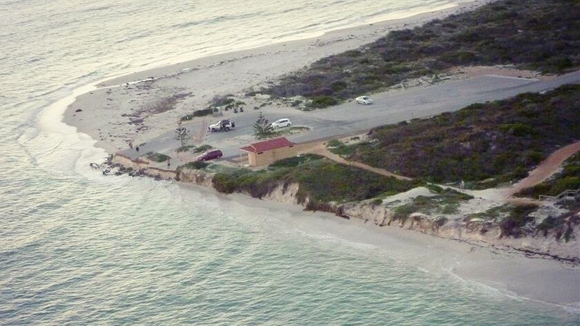 Aerial photograph of a parking lot and building right on the waterline eroded away by the ocean.