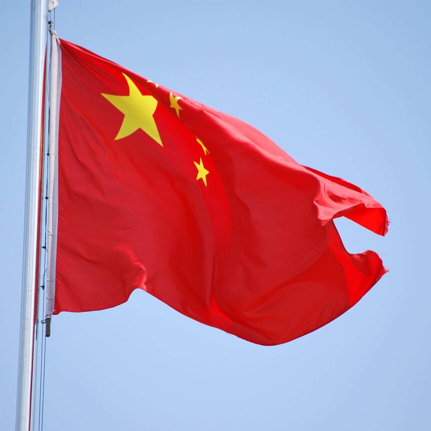 A Chinese flag on a flagpole flaps in the breeze