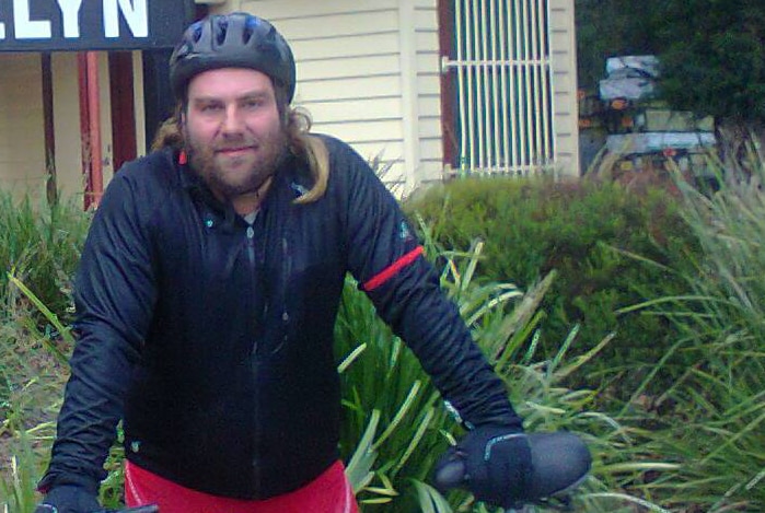 A bearded man stands next to a bicycle.