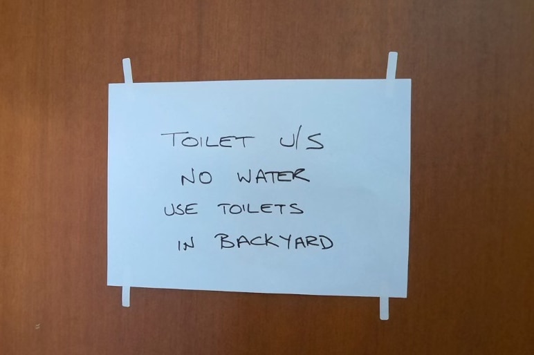 A sign is posted on a wooden toilet door, toilet no water use toilets in backyard.