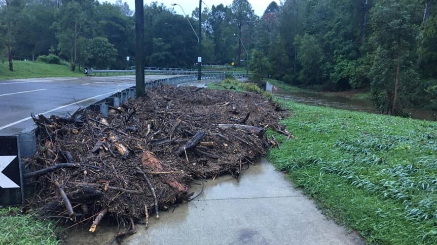 A footpath is blocked by a mass of debris washed against a guardrail by flash flooding.