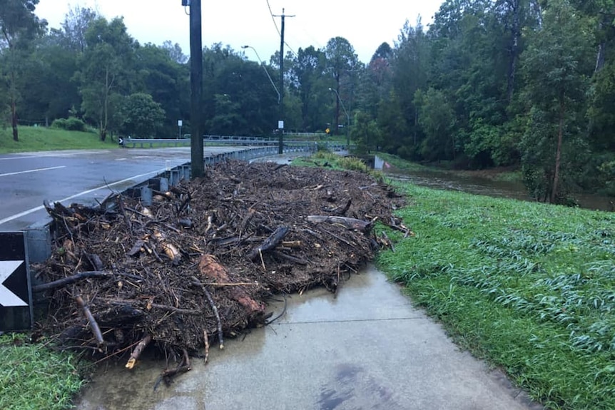 A footpath is blocked by a mass of debris washed against a guardrail by flash flooding.