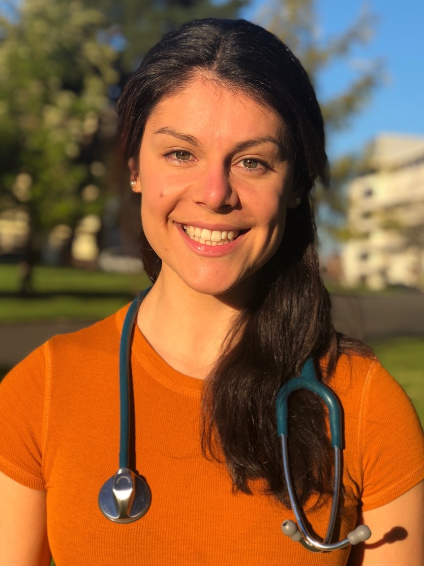 Smiling white woman with long dark hair, wearing an orange t-shirt and a stethoscope around her neck