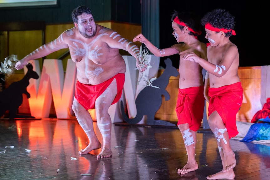 An aboriginal man and two boys in cultural paint on stage