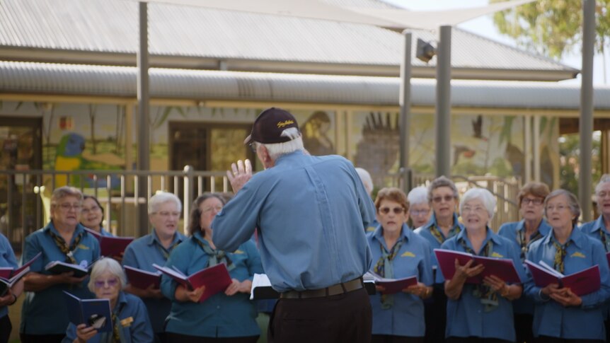 A choir sings from their songbook in front of the conductor