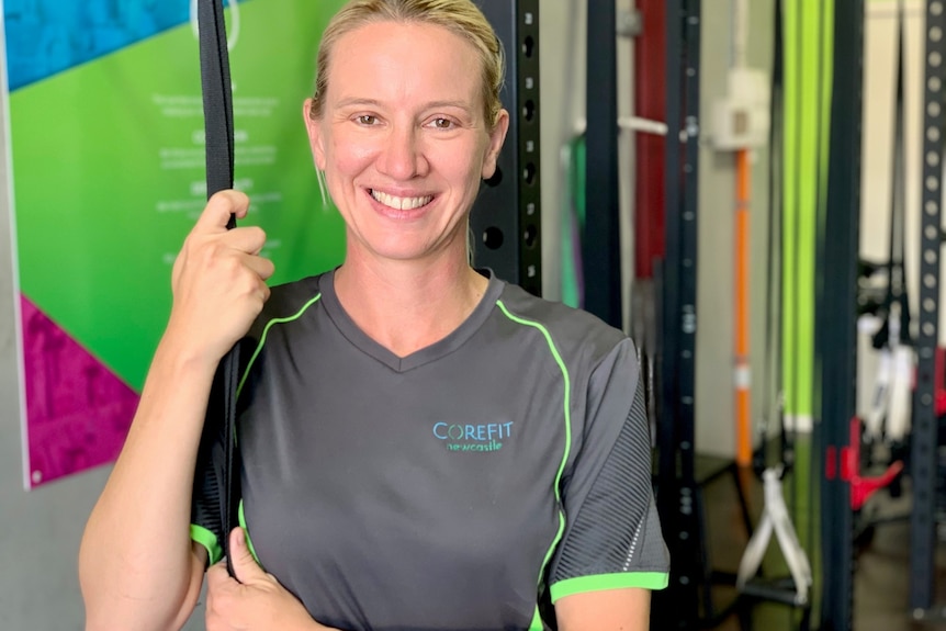 Alison Marshall holding on to ropes in her gym and smiling at the camera