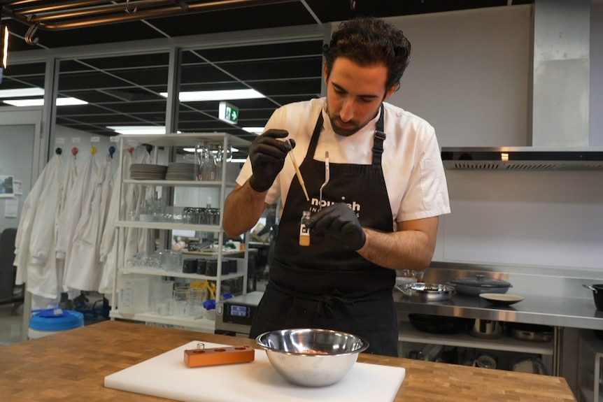 Image of a chef injecting a yellow liquid into a bowl.