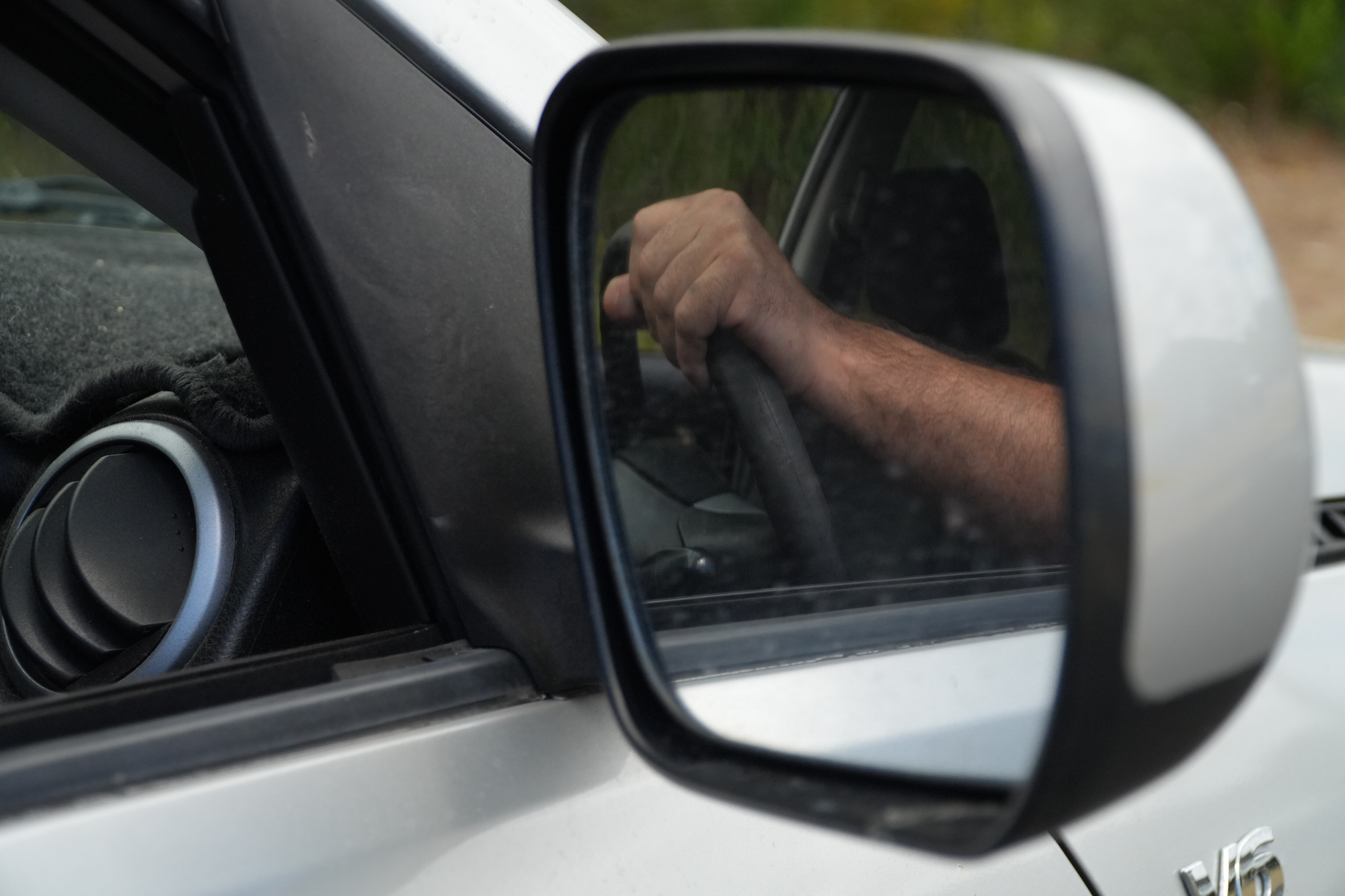 A wing mirror on a car showing a hand on a driving wheel in the reflection.