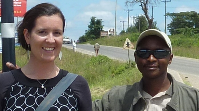 Jen Bond standing with her African driver in front of a sign that says Kenya is on the Equator