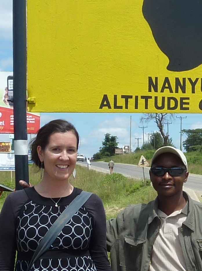 Jen Bond standing with her African driver in front of a sign that says Kenya is on the Equator
