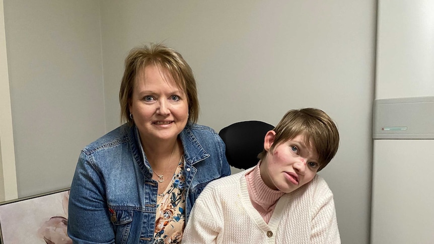 A woman sits next to her daughter who is in a wheelchair