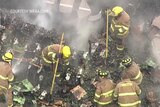 Firefighters walk among crates full of blackened and smoking avocados.