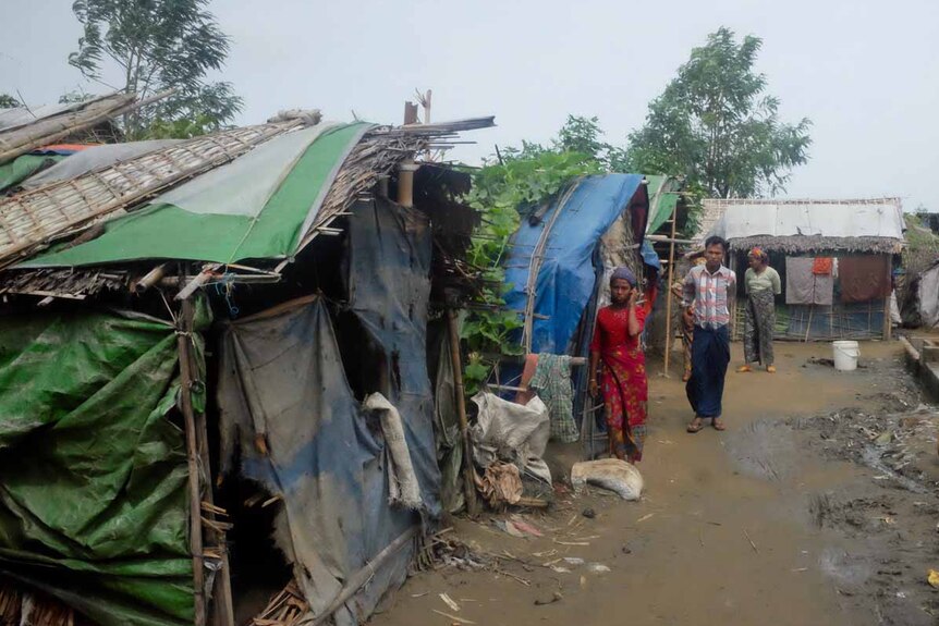 Rohingya walk past run-down houses at an unregistered camp outside Sittwe.