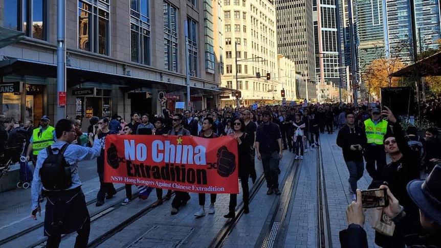 Thousands of people march down a city street holding a sign that reads "No China Extradition".