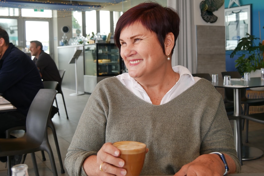 A woman looks off camera while sitting in a cafe and holding a coffee