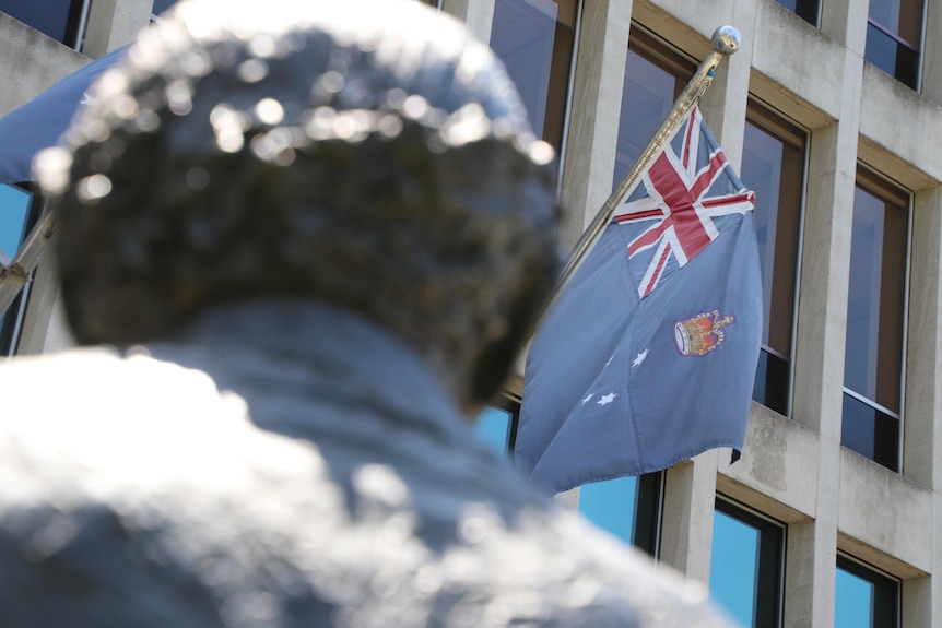 The Victorian flag flies at a government building behind a bronze statue.