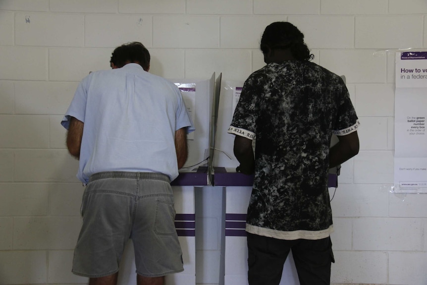 Two voters at a cardboard polling booth.