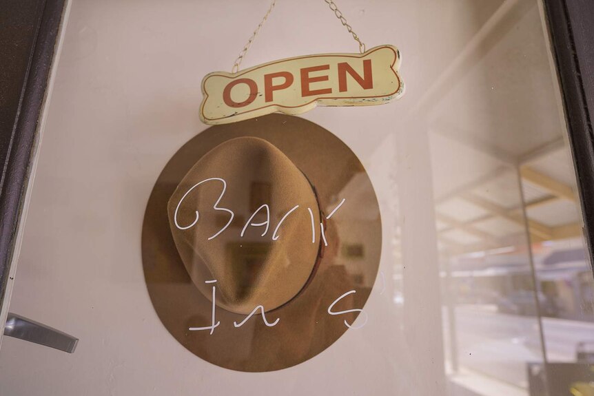 The words 'back in five' are written in white texta on a glass door with an 'Open' sign hanging above it.