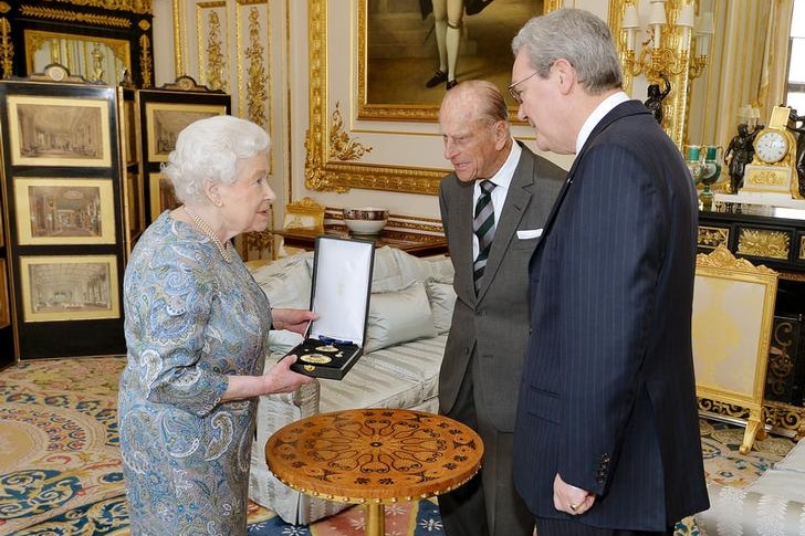 Queen Elizabeth stands to the left as she holds a box with a medal in it with Prince Philip in middle, Alexander Downer right.