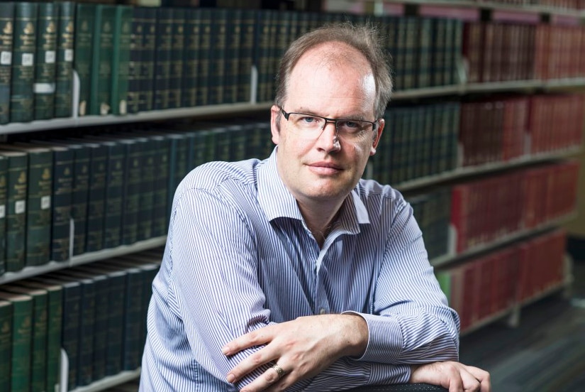 Man leans on a chair in a library.