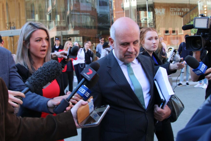 Lawyer Steven Penglis, surrounded by journalists with microphones, walking outside the City of Perth library.