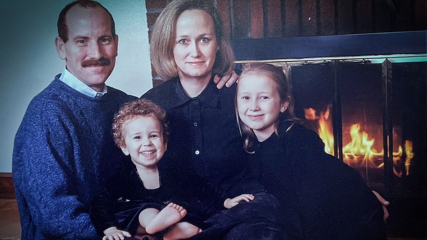 A family portrait of a man and woman with two girls on their laps in front of a fireplace 