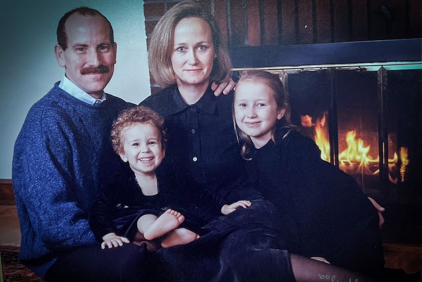 A family portrait of a man and woman with two girls on their laps in front of a fireplace 