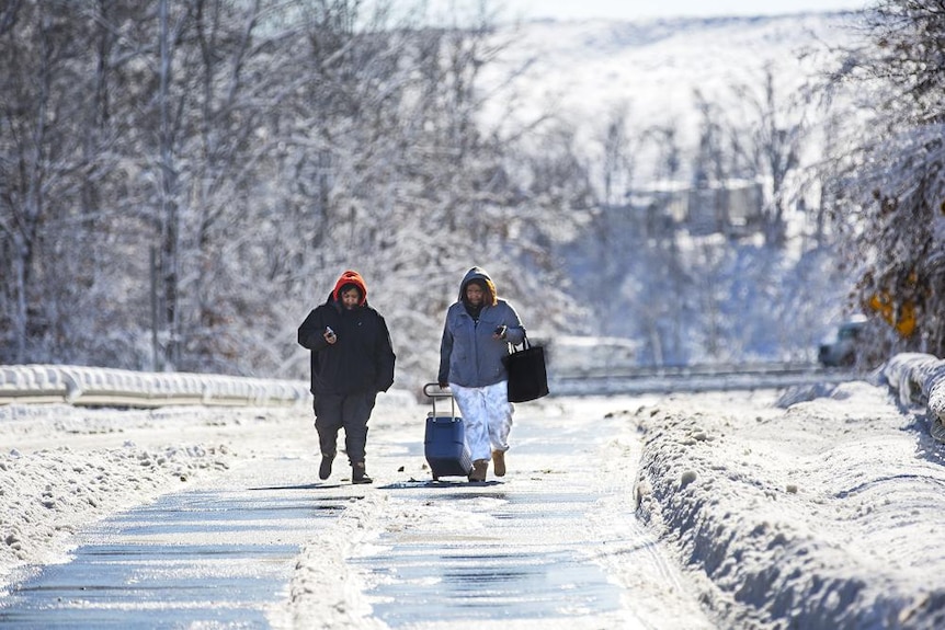 Two people walk up a snow covered ramp towards a highway in winter weather 