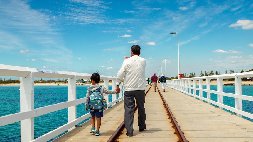 A man and a child walk along a long wooden jetty.